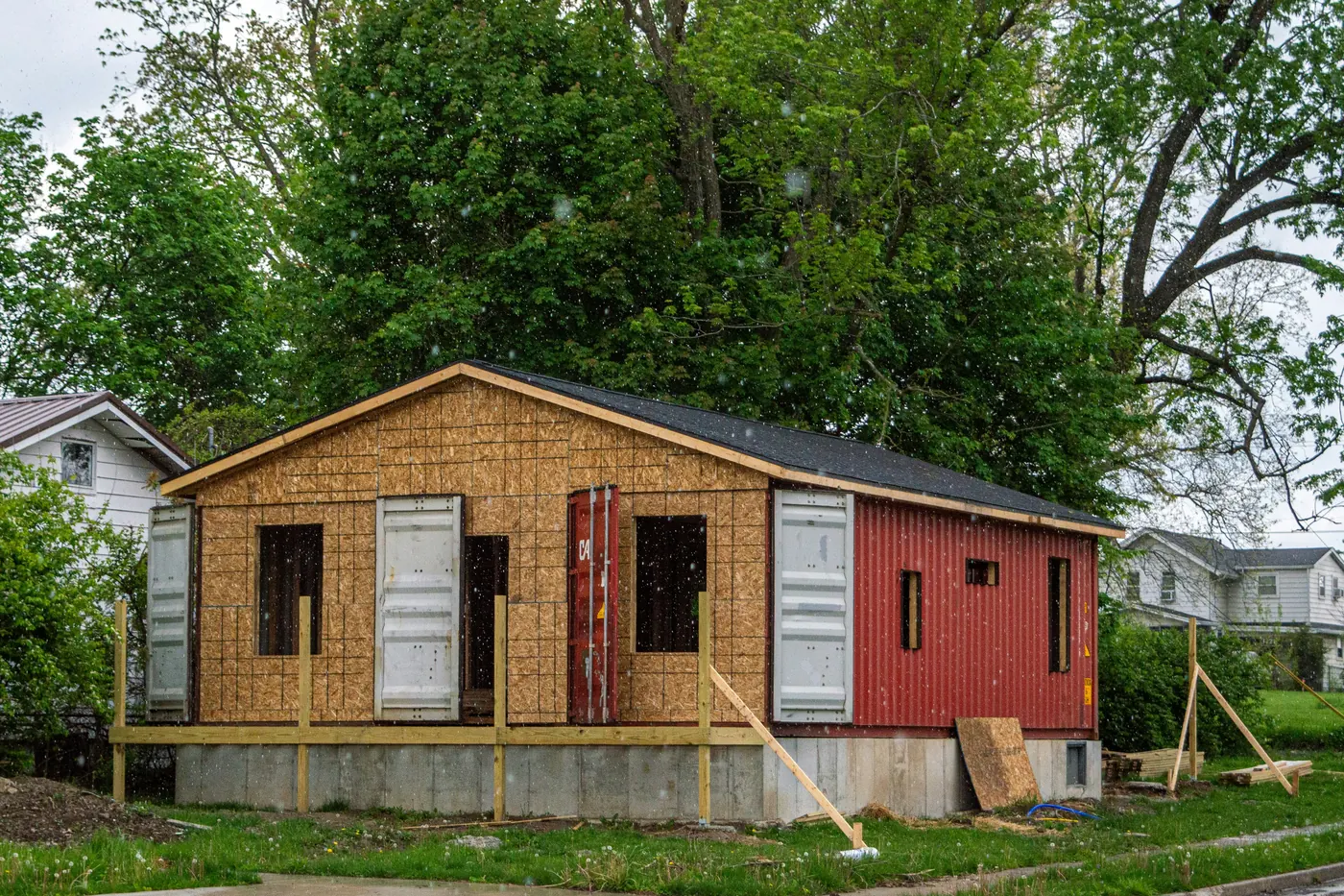 Small house under construction on a concrete foundation wall, with a large leafy tree just behind it
